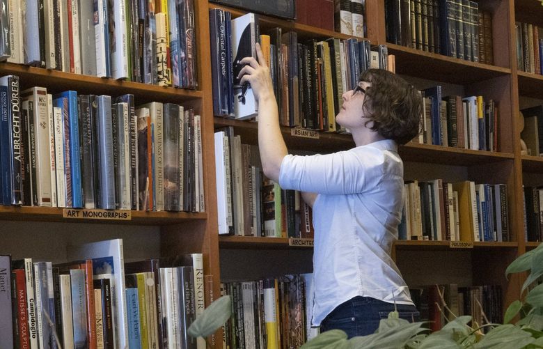Jessica Hurst, owner of Mercer Street Books in Seattle, organizes books on a shelf in her Lower Queen Anne store Friday, August 19, 2022.  She said that the feeling she tries to bring to the store is to have customers feel as though they are in a living room or a library, not a store. 221274