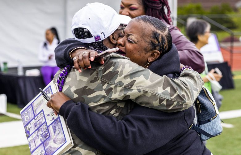 Class of 1990 student Jacqualine Hicks Boles, right, hugs her friend, Signe West, tightly as she holds a 1987 yearbook at Garfield High School’s centennial celebration in the Central District on Aug. 27, 2022. They said they are best friends: they described that they grew up together and  they became women together at the school.