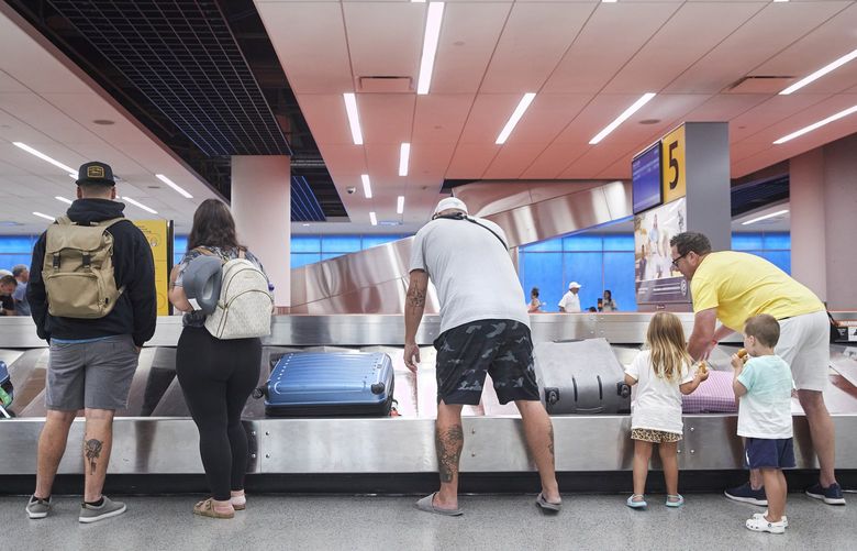 **EMBARGO: No electronic distribution, Web posting or street sales before 3 a.m. ET on Monday, Aug. 8, 2022. No exceptions for any reasons. EMBARGO set by source.** FILE – Flyers reclaim their baggage at John F. Kennedy International airport in New York, July 29, 2022. Many higher income households have been able to keep spending even as costs climb, but data and anecdotes suggest that lower-income households, despite the resilient job market, are struggling more profoundly with inflation. (Gus Powell/The New York Times)