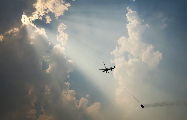 A helicopter carries a water bucket while battling the McKinney Fire, Tuesday, Aug. 2, 2022, in Klamath National Forest, Calif. (AP Photo/Noah Berger)