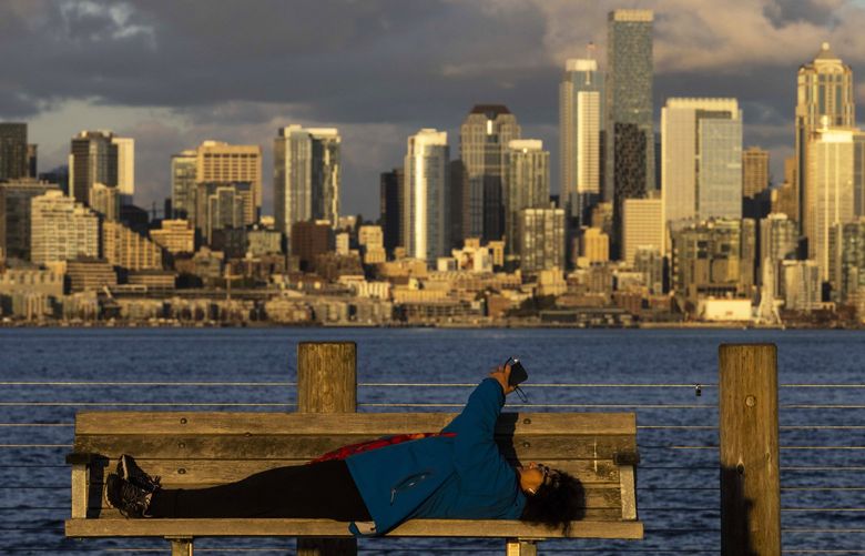 Susan Rich, of West Seattle, rests while sending a message on her phone on a bench during sunset at Alki Beach Pier in West Seattle on Monday, Oct. 11, 2021. She describes walking a long stretch of Alki and feeling accomplished by the time arriving to the viewpoint.  218504 LO