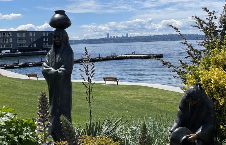 Downtown Seattle peeks over Lake Washington from behind a statue in Kirkland’s David E. Brink Park.