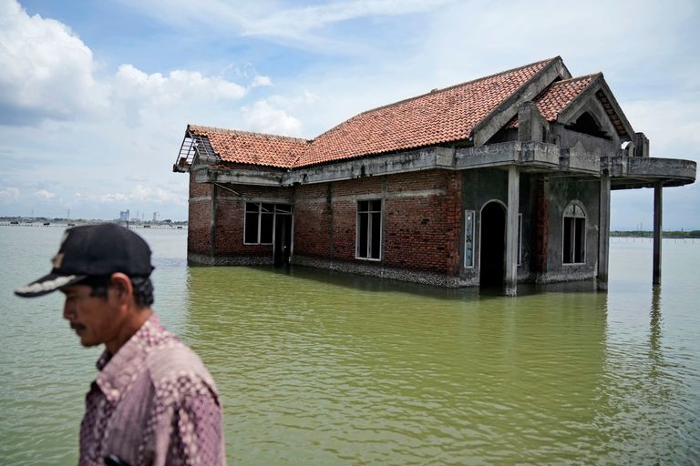 A man walks past a house abandoned after it was inundated by water due to the rising sea level in Sidogemah, Central Java, Indonesia