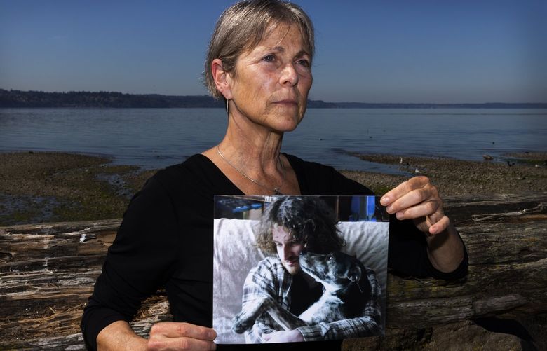 Miriam Lerner holds a photo of her son Nathan Lerner with the family dog Tessa, Monday, Aug. 15, 2022 at Saltwater State Park in Des Moines. Nathan died by suicide in Washington in 2021 and was addicted to heroin and other opioids since around age 22. Lerner and her husband Kenny, who wasn’t able to be in the portrait, live in Upstate New York and were visiting the area. Miriam said this photo is from when Nathan is around 28, two years before taking his life.