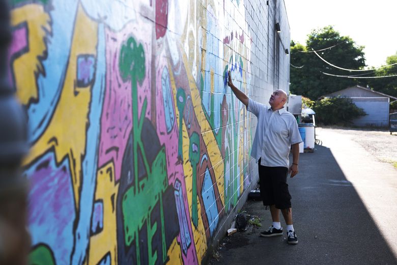 Mark Mendez touches a mural called “We Are Lake City” by Lake City youth in August. The community leader has spearheaded a street-art campaign that’s led to the creation of dozens of murals in Lake City. “I can’t paint or draw,” he said. “But I know the power of art.” (Daniel Kim / The Seattle Times)