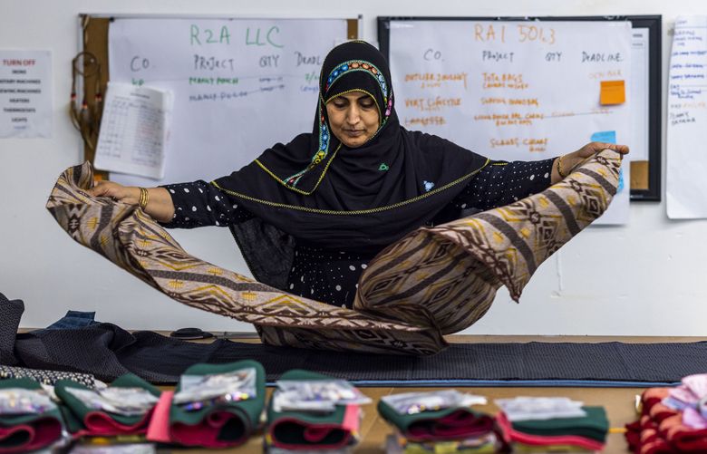 Basheerah Salim spreads fabric to make a tote at The Refugee Artisan Initiative in Lake City on Sept. 1, 2022. Salim came to the United States in 2003 and has six children.  (Daniel Kim / The Seattle Times)