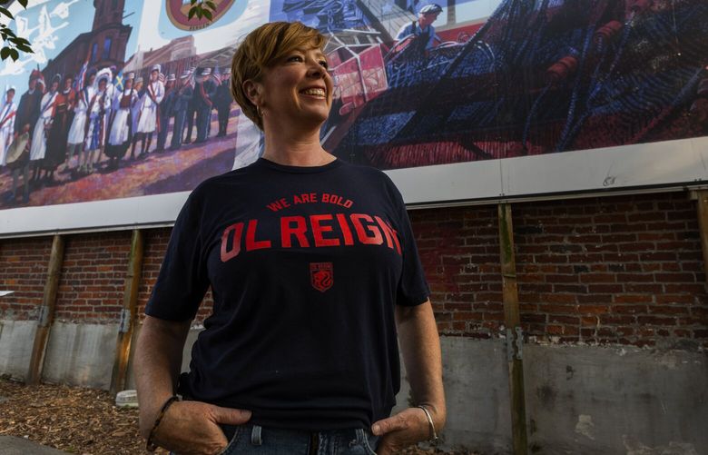 Jen Barnes, the owner of Rough & Tumble, is pictured in the Historic Ballard District, Wednesday, Sept. 14, 2022 in Seattle. Barnes will soon open a bar highlighting women’s sports. In the background is “The Mural at Bergen Place,” which celebrates Ballard’s Nordic heritage.