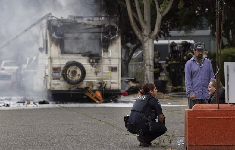 A Seattle police officer speaks with Marty Robinson as he sits, obviously upset, as his home burns in the background at the intersection of 5th Ave. S. and S. Brandon St. in Seattle’s SODO neighborhood Friday, September 16, 2022. Robinson lived in the motorhome with his cat and according to several witnesses his ex-girlfriend poured gasoline on the vehicle and set it on fire when he and his cat were inside. Unfortunately, his cat did not make it out. 221583