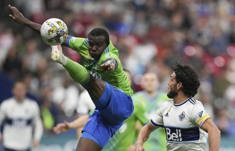 Seattle Sounders’ Nouhou Tolo, left, leaps but fails to prevent a pass from reaching Vancouver Whitecaps’ Russell Teibert during the second half of an MLS soccer match Saturday, Sept. 17, 2022, in Vancouver, British Columbia. (Darryl Dyck/The Canadian Press via AP) VCRD214 VCRD214