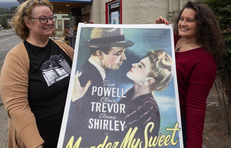 Beth Burrows, left, the owner of the North Bend Theater and manager Britni Larson display a recent Noir film shown here, Thursday, Sept. 15, 2022 in North Bend. Posting birthday messages on the marquee offer the theater an additional revenue stream.