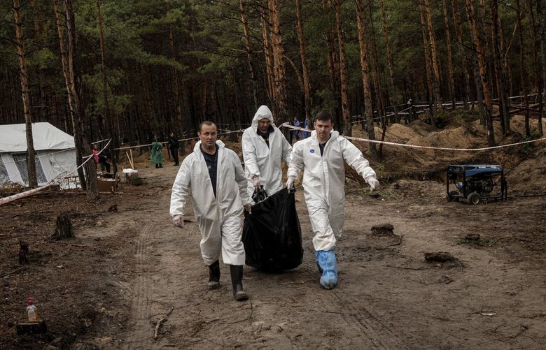 Workers move recently exhumed bodies at the mass grave site where police report that approximately 457 bodies of Ukrainian civilians and soldiers have been recovered, in Izium, Ukraine, on Friday, Sept. 23, 2022. A United Nations-appointed panel of independent legal experts said Russian soldiers raped and tortured children, executed civilians and attacked without distinguishing between civilians and combatants during the invasion of Ukraine. (Nicole Tung/The New York Times) XNYT34 XNYT34