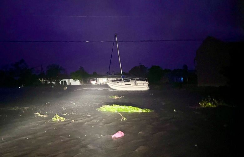 A displaced boat sits beside the roadway in the southeast corner of Cape Coral on Wednesday night, Sept. 28, 2022,  as the winds of Hurricane Ian continue to strike the flood-soaked streets. (Douglas R. Clifford/Tampa Bay Times via AP) FLPET801 FLPET801