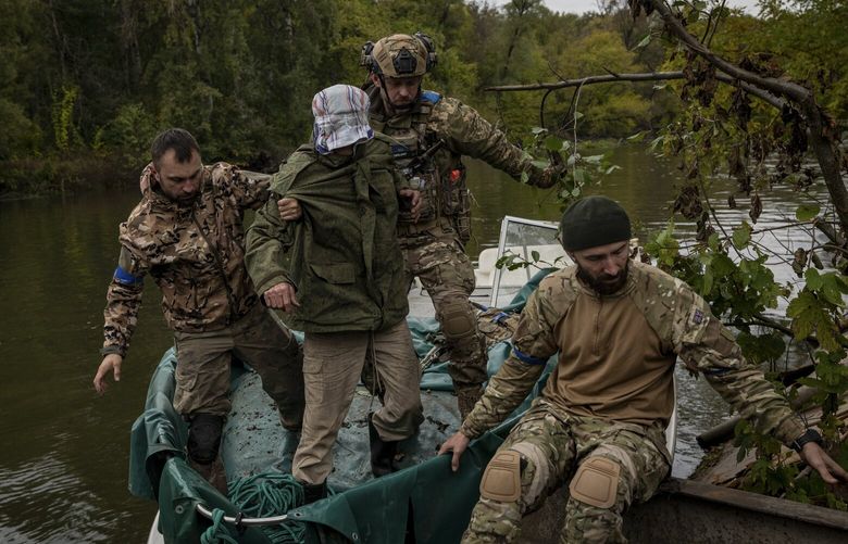 Ukrainian soldiers escort a captive, captured on the frontline and believed to be a spy for Russian forces, from a boat onto to the west bank of the Siverskyi Donets River,  near Lyman, Ukraine, on Tuesday, Sept. 27, 2022. Ukrainian forces recaptured the resort village of Szczurowe, on the eastern side of the Siverskyi Donets River, 10 days ago, and are attempting to recapture the town of Lyman from the south and western sides. (Nicole Tung/The New York Times) XNYT22 XNYT22