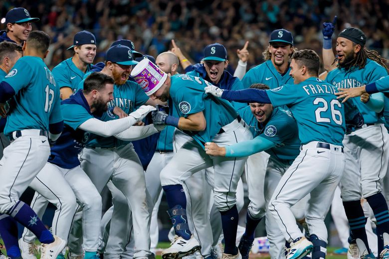 Teammates swarm Seattle Mariners catcher Cal Raleigh after Raleigh hit a walk-off home run to beat the Oakland Athletics 2-1 and secure the Mariners first post season berth in 21 years. 221659 (Jennifer Buchanan / The Seattle Times)