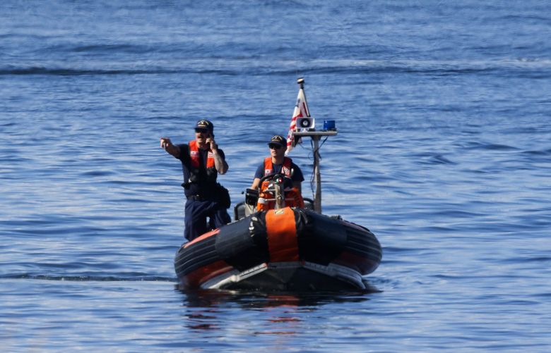 U.S. Coast Guard personnel seen through heatwaves over the waters of Mutiny Bay search the shore on the west side of Whidbey Island, Monday late morning, Sept. 5, 2022 after Sunday’s fatal floatplane crash.
