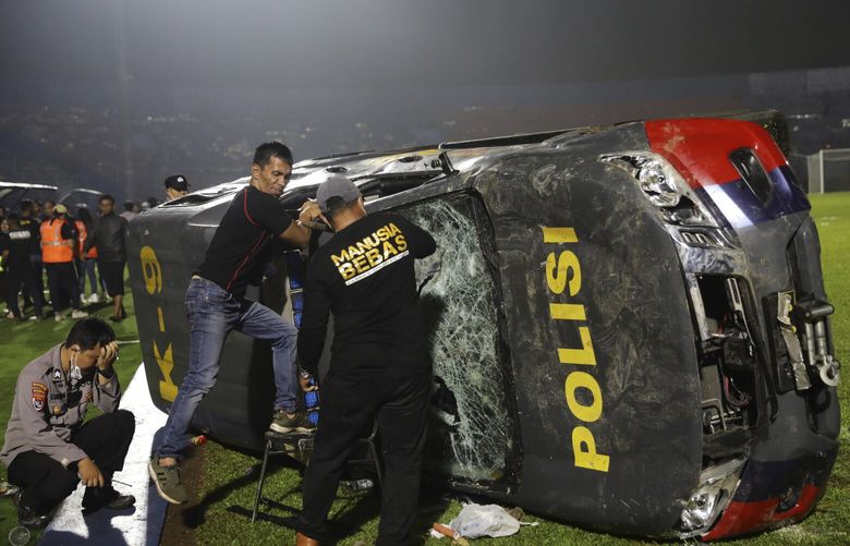 Officers examine a damaged police vehicle following a clash between supporters of two Indonesian soccer teams at Kanjuruhan Stadium in Malang, East Java, Indonesia, Saturday, Oct. 1, 2022. Panic following police actions left over 100 dead, mostly trampled to death, police said Sunday. (AP Photo/Yudha Prabowo) XJAK107 XJAK107