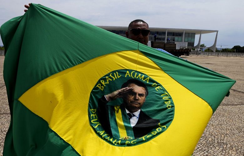 A supporter of Brazilian President Jair Bolsonaro, who is running for reelection, waves a flag with this image the day after presidential elections lead to a second round, outside Planalto presidential palace in Brasilia, Brazil, Monday, Oct. 3, 2022. The second round of the Brazilian elections takes place on Oct. 30. (AP Photo/Eraldo Peres) XEP103 XEP103