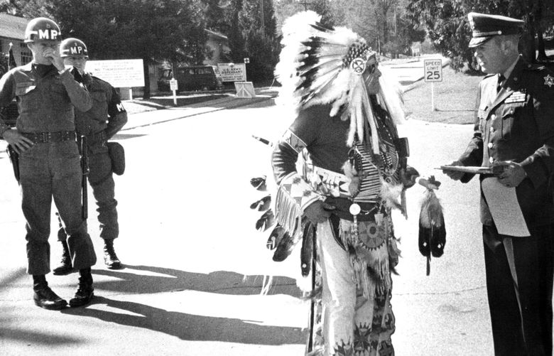 Chief Confers Title On Lawton Commander
Chief White Buffalo Man, grandson of Sitting Bull, yesterday gave Fort Lawton’s commander, Col. Stuart J. Palos, a new title: Kangee-Saihe, or Crow Foot. Military policemen looked on. Palos received the honorary title after inviting the chief inside the fort, a privilege denied other Indians who are demonstrating to dramatize their demand that part of the fort be given to the Indians. The demonstration yesterday included a “message” in the sky. (Ron De Rosa / The Seattle Times)