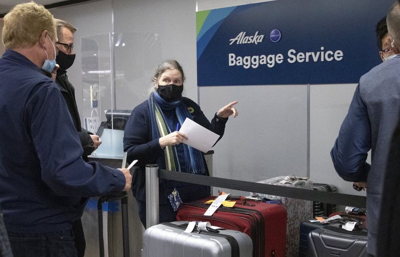 A woman at the Alaska Baggage Service area at SEA (Seattle-Tacoma International Airport) tries to help passengers with missing luggage Tuesday, December 28, 2021.  Everyone was there to try to find their luggage.  When many flights were cancelled and people were not able to board planes on Sunday and Monday, according to many frustrated passengers, often luggage was put on a later flight, without the people who owned it, and many passengers were unable to find their missing luggage Tuesday. 219198