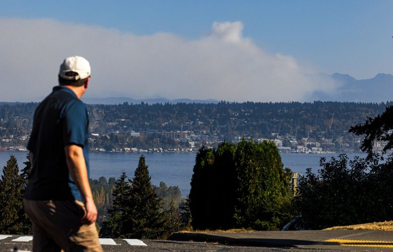 A steady column of smoke rises up into the sky behind Kirkland as a resident of Seattleís View Ridge neighborhood slows to look across Lake Washington at the Loch Katrine fire, just 30 miles away, Sunday, Oct. 16, 2022.
