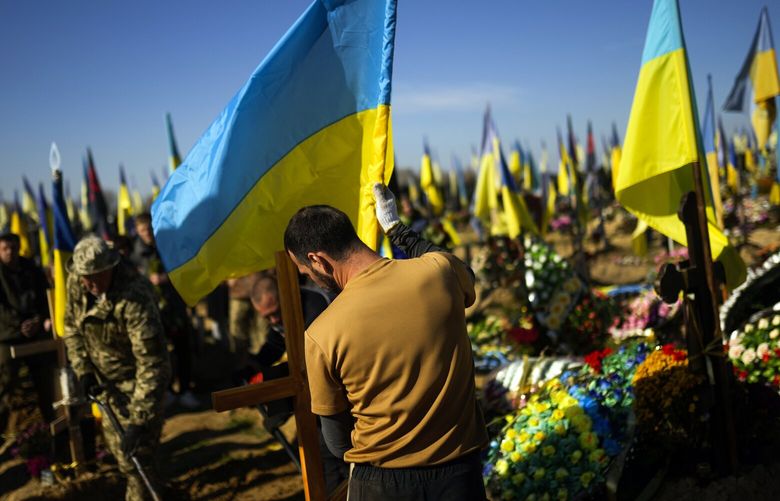 A man places a Ukrainian flag in the grave of recently killed Ukrainian serviceman Vadim Bereghnuy, 22, during his funeral in a cemetery in Kharkiv, Ukraine, Monday, Oct. 17, 2022. (AP Photo/Francisco Seco) FS112 FS112