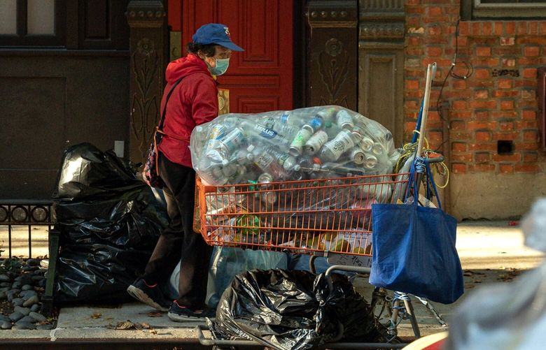 A woman collects cans and bottles from trash piled on the sidewalk along Downing Street in the Greenwich Village neighborhood of New York on Oct. 14, 2022. With both trash and rat complaints on the rise and concerns that the city is looking filthier than it has in decades, sanitation officials have come up with a potential solution they hope will help clean up the streets. (Emon Hassan/The New York Times)