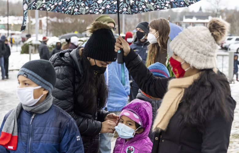 Angelica Lopez, back center, fixes her daughter Gretel Gonzalez Lopez’s mask as Angelica’s sister Rosa Lopez holds an umbrella while they all wait in line to get rapid antigen COVID tests for their children, who all attend Concord International School in South Park, on Sunday, Jan. 2, 2022. Seattle Public Schools and their testing partner, Premier Medical Group, were providing the tests on Sunday at South Shore PreK-8 in Rainier Beach.

School will be closed Monday, Jan. 3 as widespread rapid COVID testing will happen again at 12 middle school locations from 1 to 4 p.m.