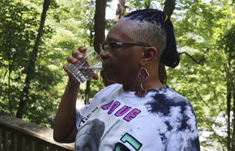 Donna Dickerson drinks a cup of tap water on the porch of her trailer in Keystone, W.Va., on June 22, 2022. For about a decade before being hooked up to a new water system late last year, residents of Keystone like Dickerson were told to boil water before drinking it for a decade because of the community’s aging infrastructure. (AP Photo/Leah Willingham) CLI102 CLI102