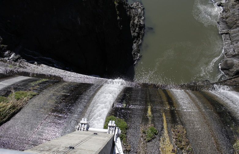 FILE – Excess water spills over the top of a dam on the Lower Klamath River known as Copco 1 near Hornbrook, Calif., on March 3, 2020. Plans for the largest dam demolition project in U.S. history to save imperiled salmon could soon become reality, with the first stages of construction starting in California as early as this summer. The Federal Energy Regulatory Commission meets Thursday, Nov. 17, 2022, and is expected to vote on whether to approve the surrender of PacificCorp’s hydroelectric license for four dams on the lower Klamath River in remote northern California. (AP Photo/Gillian Flaccus, File) LA304 LA304