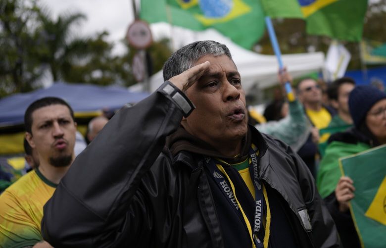 FILE – A supporter of Brazilian President Jair Bolsonaro salutes while singing the nation’s anthem outside a military base during a protest against his reelection defeat in Sao Paulo, Brazil, Nov. 3, 2022. Supporters of incumbent President Jair Bolsonaro who refuse to accept his narrow defeat in October’s election have blocked roads and camped outside military buildings while pleading for intervention from the armed forces or marching orders from their commander in chief. (AP Photo/Matias Delacroix, File) XLAT139 XLAT139