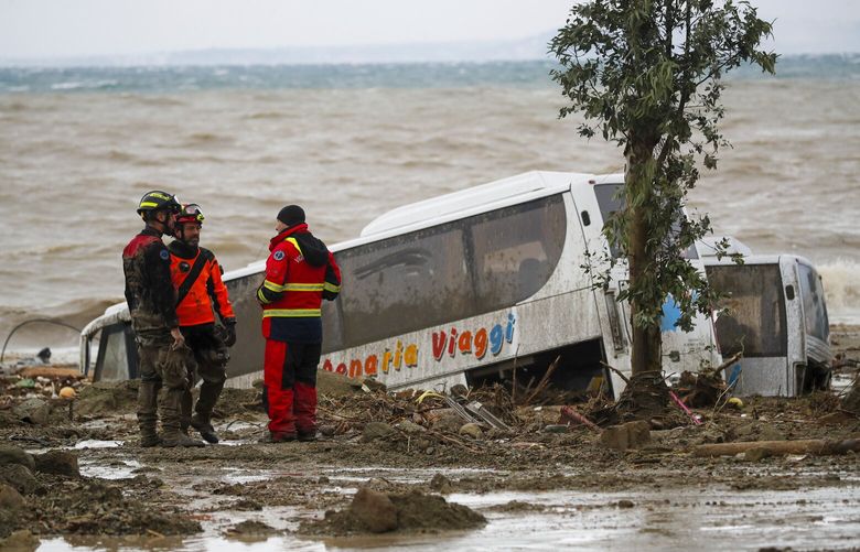 Rescuers stand next to a bus carried away after heavy rainfall triggered landslides that collapsed buildings and left as many as 12 people missing, in Casamicciola, on the southern Italian island of Ischia, Italy, Saturday, Nov. 26, 2022. Firefighters are working on rescue efforts as reinforcements are being sent from nearby Naples, but are encountering difficulties in reaching the island either by motorboat or helicopter due to the weather. (AP Photo/Salvatore Laporta) AJM102 AJM102