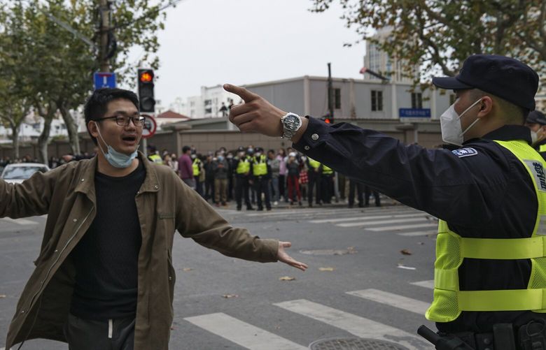 In this photo taken on Sunday, Nov. 27, 2022, a protester holding flowers is confronted by a policeman during a protest on a street in Shanghai, China. Authorities eased anti-virus rules in scattered areas but affirmed China’s severe “zero- COVID” strategy Monday after crowds demanded President Xi Jinping resign during protests against controls that confine millions of people to their homes. (AP Photo) XAW206 XAW206
