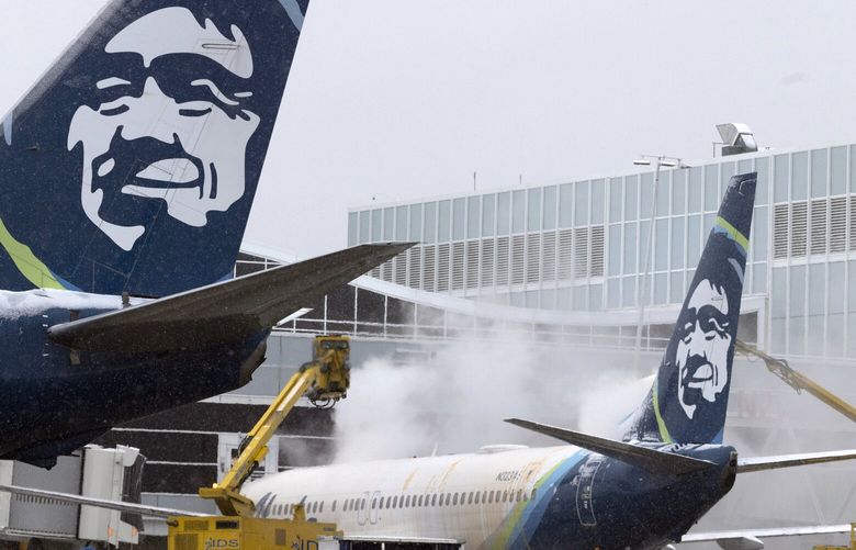 As another Alaskan airlines jet taxies by, an Alaska Airlines plane is deiced early Tuesday morning, November 29, 2022.  Over 100 Alaska flights were cancelled due to the weather. 222318