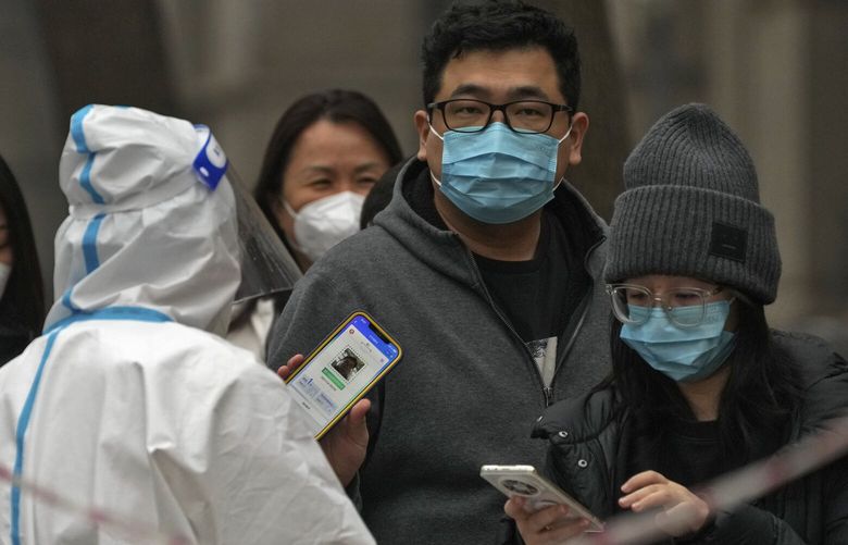 FILE – A man shows his health check QR code as he and others line up to get their routine COVID-19 throat swabs at a coronavirus testing site in Beijing, Thursday, Nov. 24, 2022. (AP Photo/Andy Wong, File) BKWS307 BKWS307