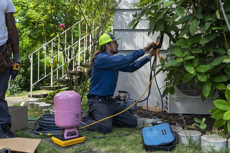 Workers install a heat pump system in June at a home in Seattle