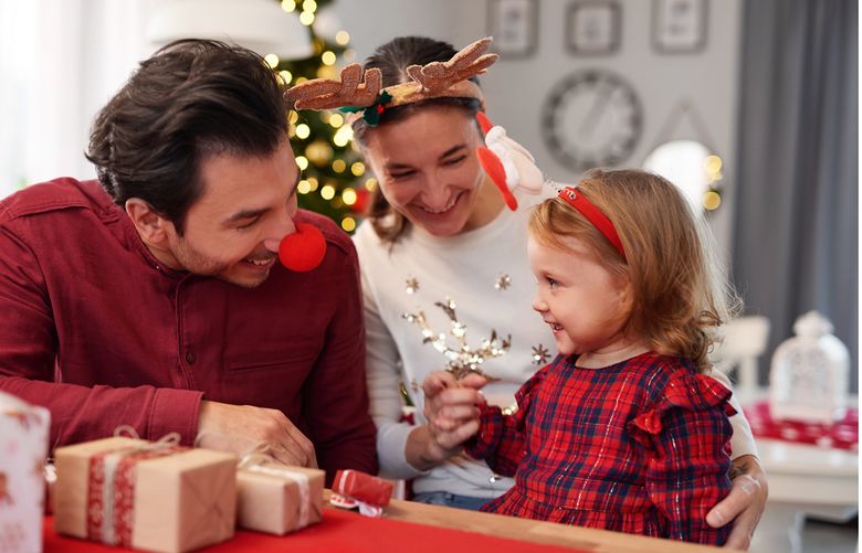A family in Christmas-garb laugh together in a living room