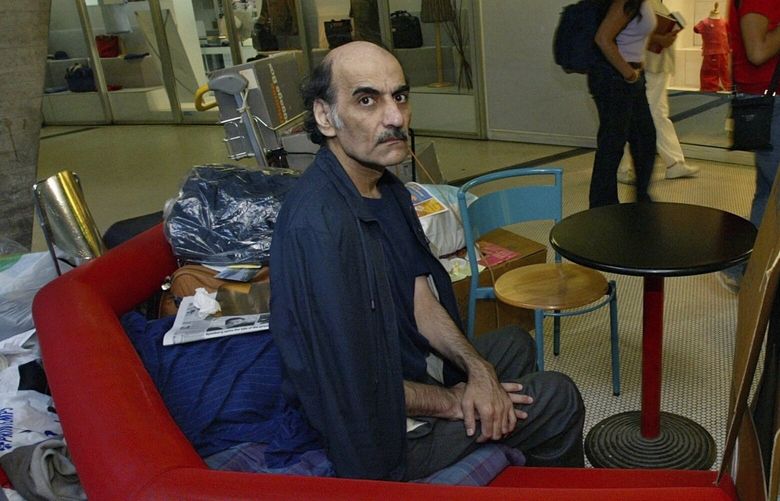 FILE – Merhan Karimi Nasseri sits among his belongings at Terminal 1 of Roissy Charles De Gaulle Airport, north of Paris on Aug. 11, 2004 . An Iranian man who lived for 18 years in Paris’ Charles de Gaulle Airport and inspired the Steven Spielberg film “The Terminal” died Saturday, Nov. 12, 2022 in the airport, officials said. Merhan Karimi Nasseri died after a heart attack in the airport’s terminal 2F around midday, according an official with the Paris airport authority. Police and then a medical team treated him but were not able to save him, the official said. (AP Photo/Michel Euler, File) XFP101 XFP101