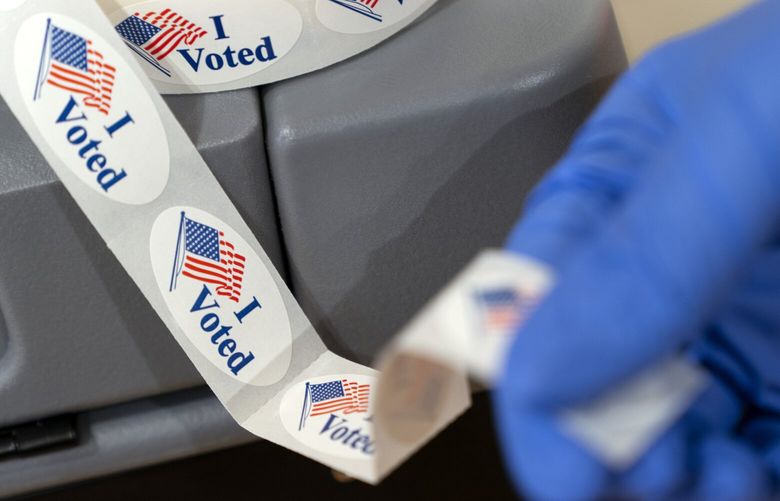 Poll worker Sheila Hawkes removes an “I Voted” sticker to hand to a voter at an early voting center at Ida B. Wells Middle School, Thursday, Oct. 29, 2020, in Washington. (AP Photo/Jacquelyn Martin)