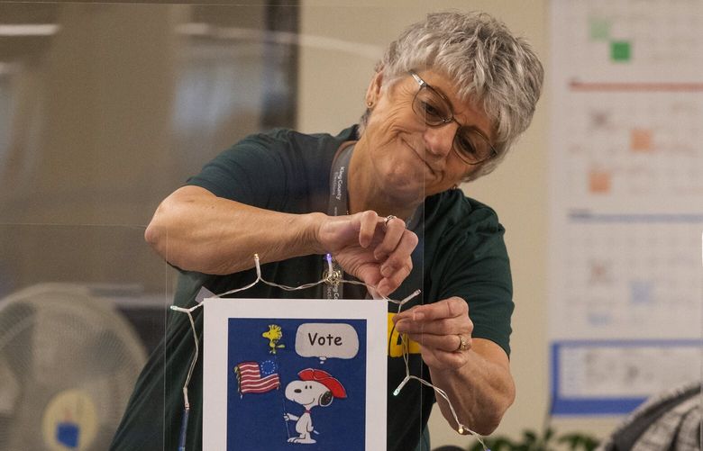 Election worker Leona Clissold hangs holiday lights at her desk on Election Day at the King County Elections headquarters, Tuesday, Nov. 8, 2022 in Renton. Clissold’s position is (ballot) opening lead and this is her 14th election worked.