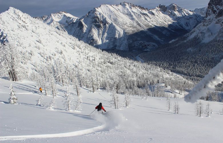 The Liberty Bell looms over Washington Pass as Justin Smith carves turns on a backcountry ski run called Portly Bowl while mountain guide Josh Cole looks on.