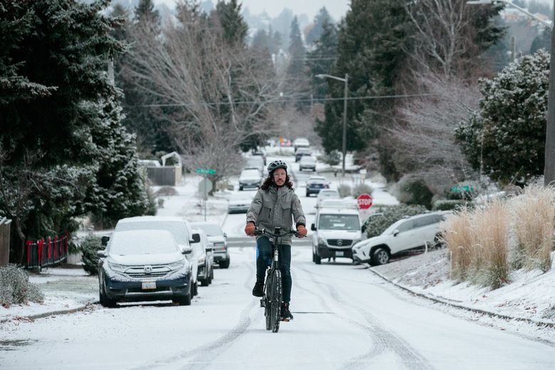 Rubin Molina rides his electric bike through the snow in West Seattle on Friday morning. (Erika Schultz / The Seattle Times)
