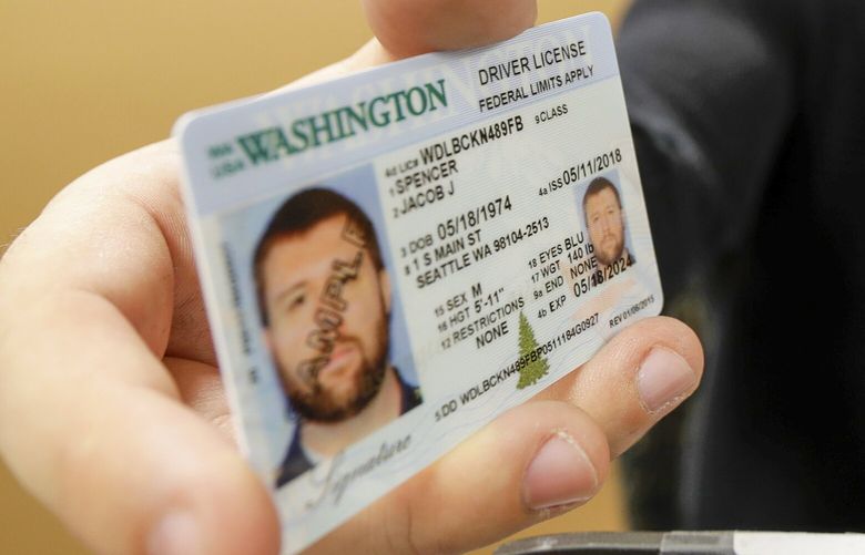 Ryan Norris, a license service representative at the Washington state Dept. of Licensing office in Lacey, Wash., poses for a photo Friday, June 22, 2018 while holding a sample copy of a Washington drivers license. Some Washington licenses and identification cards will soon be marked with the words “federal limits apply” as the state moves to comply with a federal law that increased rules for identification needed at airports and federal facilities. (AP Photo/Ted S. Warren) WATW207