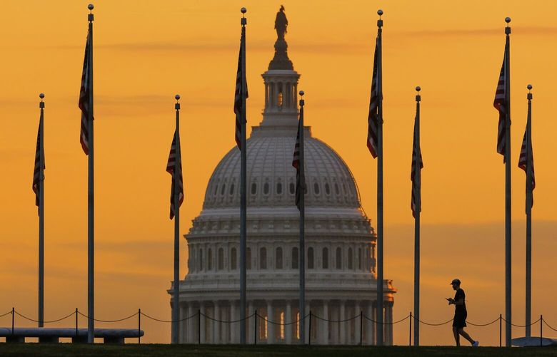 An early morning pedestrian is silhouetted against sunrise as he walks through the U.S. Flags on the National Mall and past the U.S. Capitol Building in Washington, Monday, Nov. 7, 2022, one day before the midterm election will determine the control of the U.S. Congress. (AP Photo/J. David Ake)