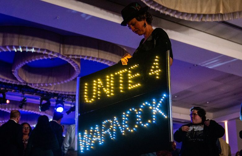 A supporters carries a sign in support of Sen. Raphael Warnock (D-Ga.) during Warnock for Georgia run-off Election Night Watch Party at the Atlanta Marriott Marquis in Atlanta, Ga., on Tuesday. MUST CREDIT: Washington Post photo by Demetrius Freeman.