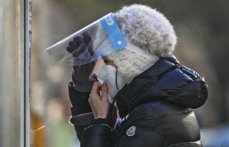 A woman wearing a face mask and face shield get ready for her routine COVID-19 throat swab at a coronavirus testing site in Beijing, Wednesday, Dec. 7, 2022. China has announced new measures rolling back COVID-19 restrictions, including limiting lockdowns and testing requirements. (AP Photo/Andy Wong) XAW107 XAW107