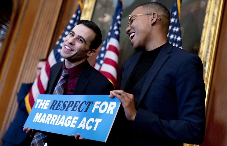 Equality Caucus Executive Director Jordan Dashow, left, and Equality Caucus Press Secretary Malachi White, right, pose with a sign that reads “The Respect For Marriage Act” after House Speaker Nancy Pelosi of Calif., accompanied by members of Congress, signed H.R. 8404, the Respect For Marriage Act, on Capitol Hill in Washington, Thursday, Dec. 8, 2022. (AP Photo/Andrew Harnik) DCAH153 DCAH153