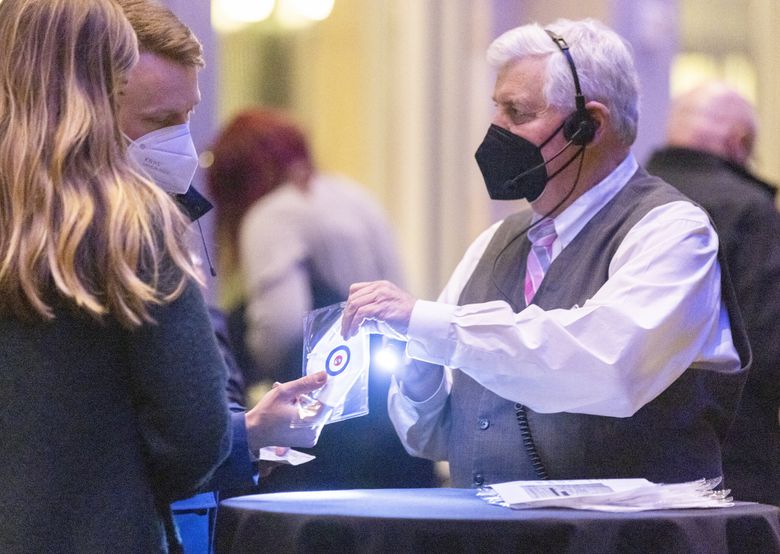 A worker checks proof of vaccination and hands over a free mask to an attendee at the Eddie Vedder & the Earthlings show at Benaroya Hall in Seattle in February. On Friday, public health and health care officials advised Washington residents to wear masks indoors as viral respiratory illness infections continue to soar. (Amanda Snyder / The Seattle Times)