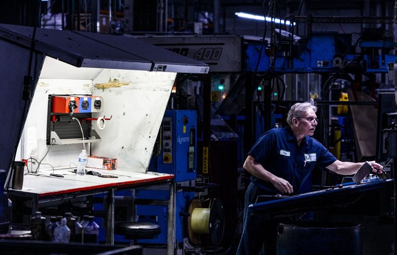 Journeyman pressman Tony Hoshaw is illuminated in light as he works on production of the first edition of the next day’s Seattle Times newspaper at a printing press in Kent on Aug. 24, 2022.
