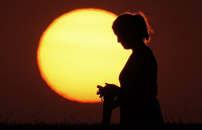 A woman is silhouetted against the setting sun at the close of a hot summer day, Monday, Aug. 1, 2022, in Kansas City, Mo. Sunsets in the midwest have been more vibrant than usual lately because of smoke from western wildfires in the atmosphere. (AP Photo/Charlie Riedel)