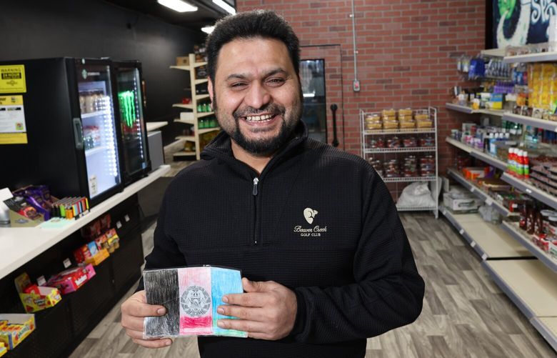 Wahidullah Qaderdan, co-owner at Mart at Main, holds up a drawing of an Afghanistan flag his daughter made in Renton on November 26, 2022. Qaderdan, who fled Afghanistan in 2019, would like to convert his store into a restaurant that serves Afghan dishes. He is grateful for the help he received from Hopelink in learning to speak English, especially Giles Bohannon and Kelli Graham, “Those two people are rockstars,” he said. He dreams of starting a charity in Afghanistan that can supply people with food and clothing.